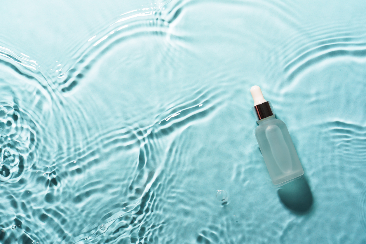A frosted skincare dropper bottle on rippled turquoise water