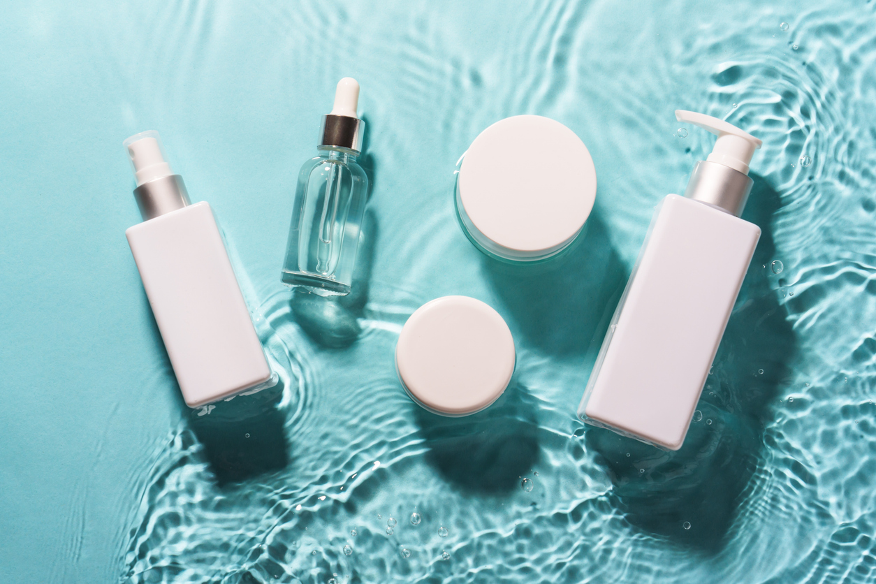 A set of white skincare bottles and jars arranged on rippled turquoise water